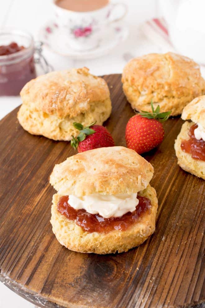 4 English Scones on a board with one sandwiched with jam and clotted cream