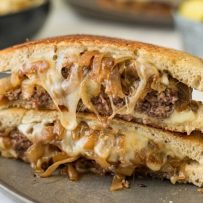A patty melt cut in half and stacked on top of each other to show melted cheese and onions