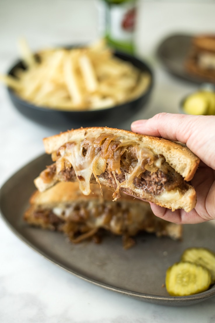 A hand holding half of a patty melt just before taking a bite