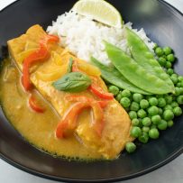 A complete meal in a black bowl, salmon in curry sauce with peas, slow peas and white rice.