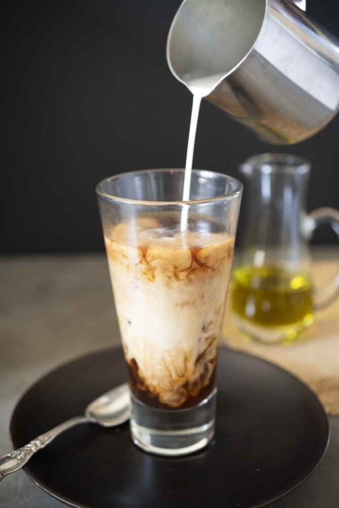 A tall glass of coffee pouring in milk
