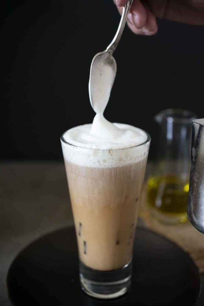 Using a spoon to add milk foam to a tall glass of iced coffee