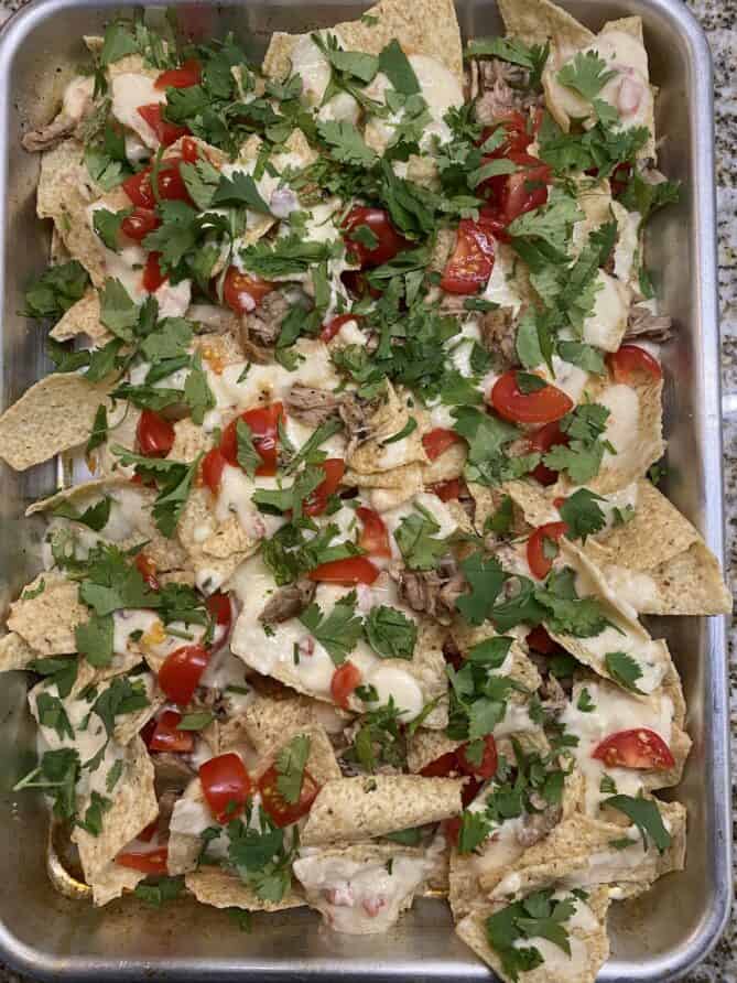 A baking pan full of nachos with queso, tomato, pulled pork and cilantro