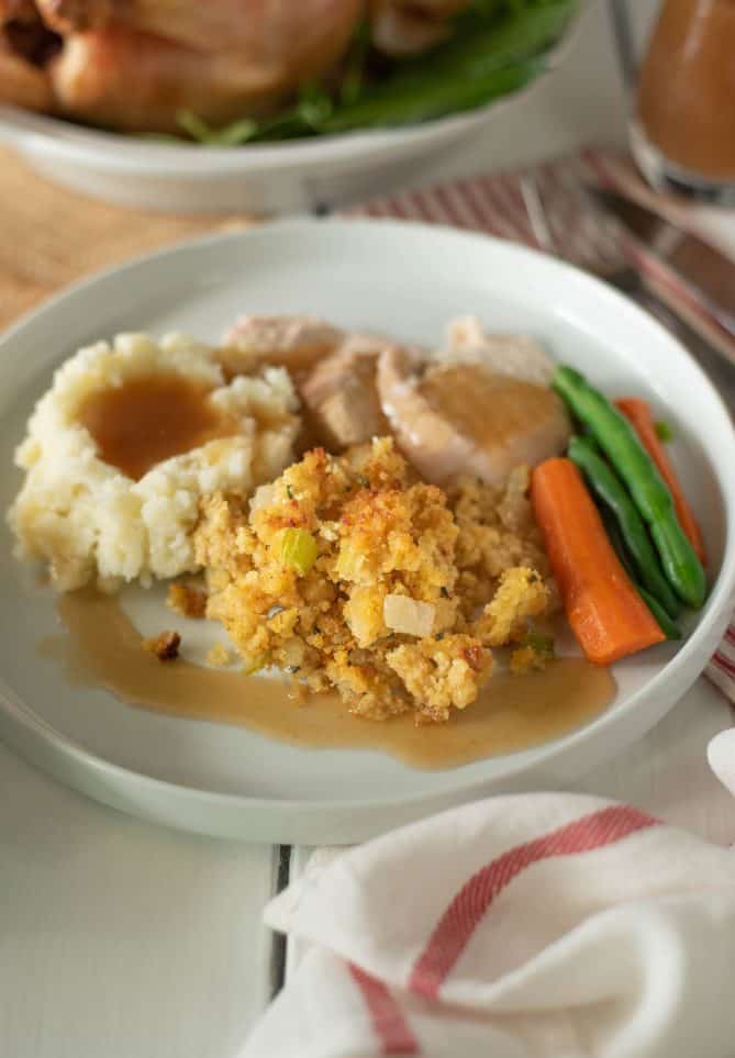 A white plate with sliced turkey, gravy, carrots, green beans, mashed potato and stuffing