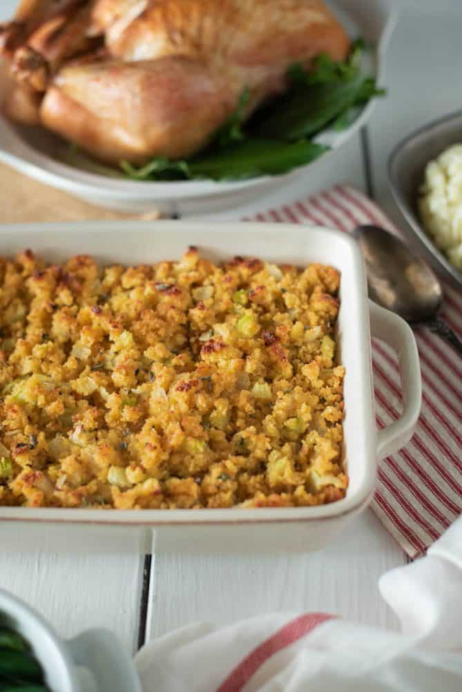 Cornbread, sage & onion stuffing in a roasting pan with a roast turkey behind