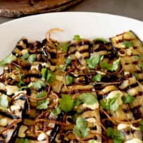 Coronation aubergine/eggplant slices fanned out on a serving platter with fried crispy onions