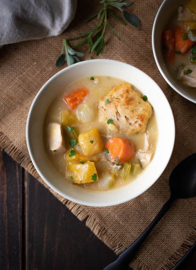 Creamy chicken stew with sage and chive dumplings in a bowl with a spoon