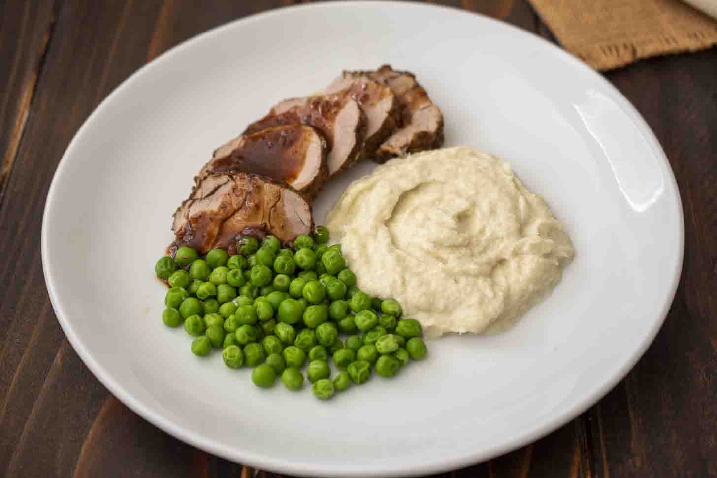 A plate of sliced pork, green peas and fennel puree