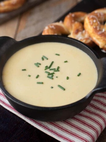 A black cast iron soup bowl filled with beer cheese soup, garnished with chopped chives and served with soft pretzels