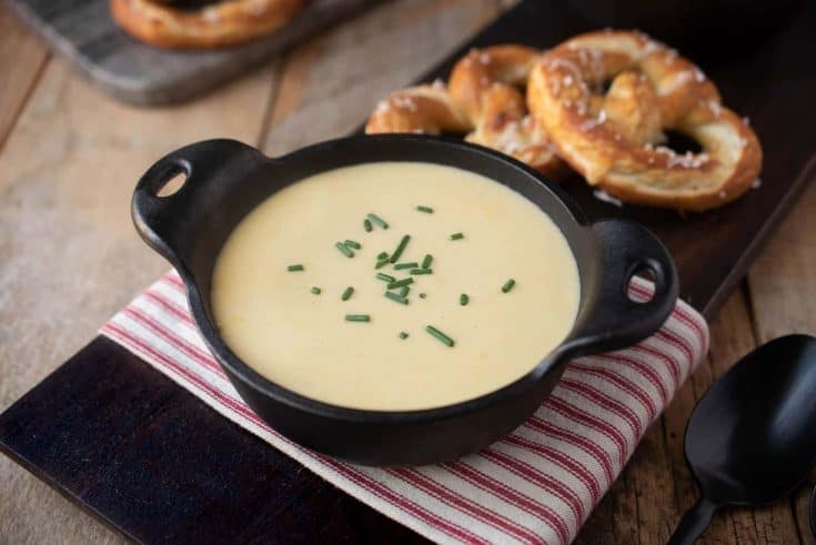 A black cast iron soup bowl filled with beer cheese soup, garnished with chopped chives and served with soft pretzels