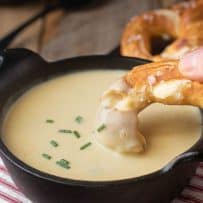 A closeup of dunking a soft pretzel into creamy beer cheese soup with chopped chives