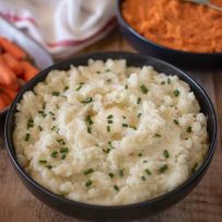 Creamy microwave mashed potatoes in a black bowl topped with chives, carrots and mashed sweet potato
