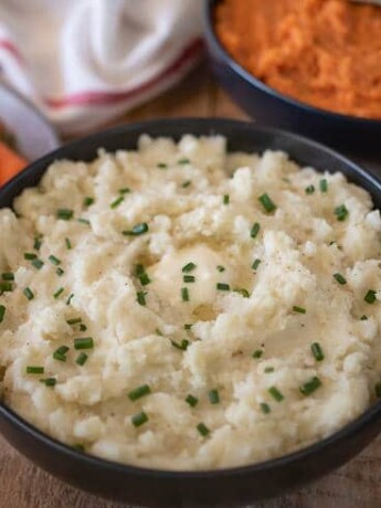 Creamy microwave mashed potatoes in a black bowl topped with chives, carrots and mashed sweet potato