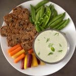 A selection of colorful vegetables and crackers with a bowl of creamy tzatziki dipping sauce