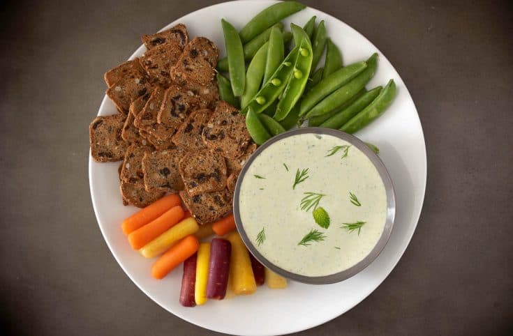 A selection of colorful vegetables and crackers with a bowl of creamy tzatziki dipping sauce