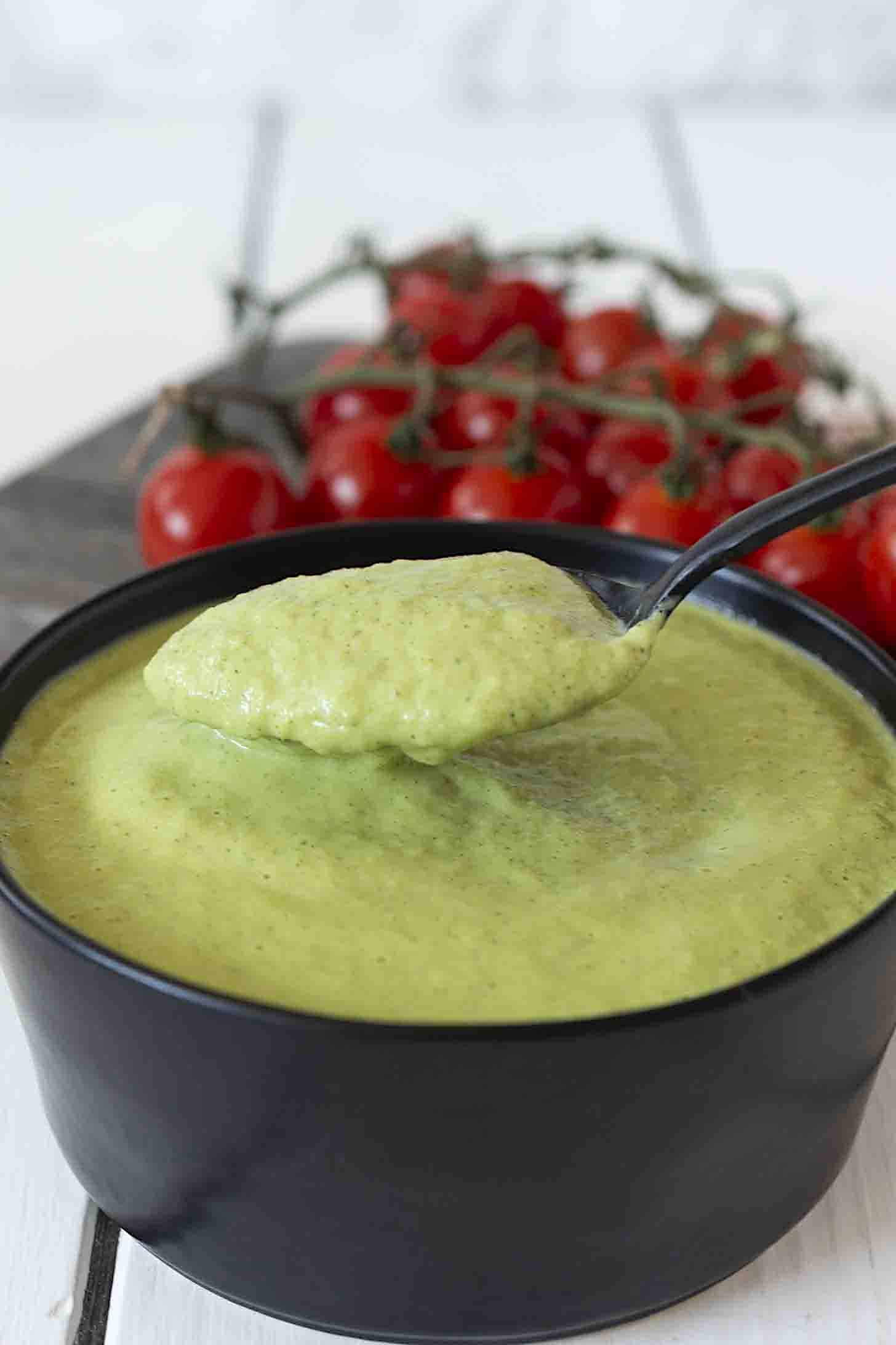 A black bowl of vibrant green zucchini sauce with a black spoon