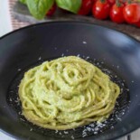 Spaghetti swirled on a black plate with green pasta sauce