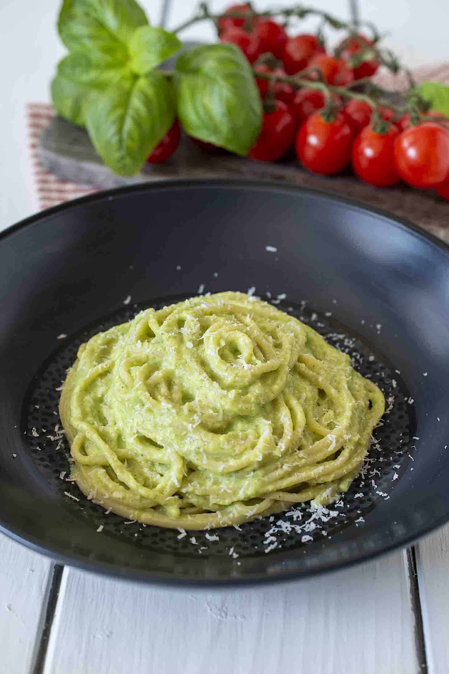Spaghetti swirled on a black plate with green pasta sauce