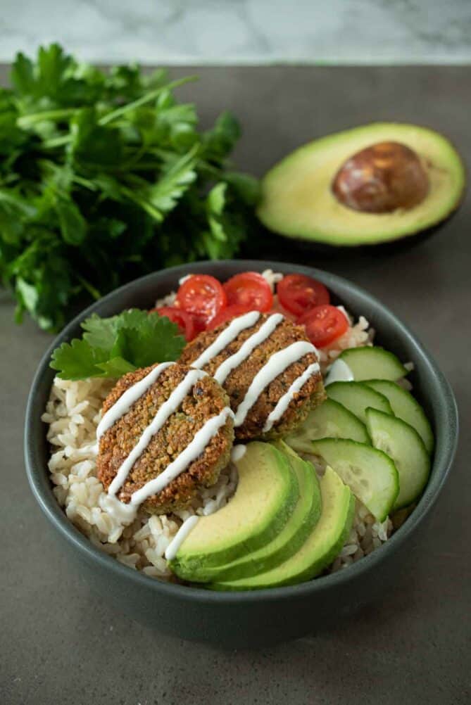 Rice, avocado, cucumber, tomato and falafel in a bowl topped with yogurt sauce