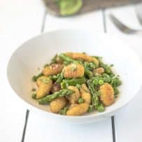 Green asparagus and peas with crispy gnocchi in a white bowl
