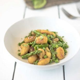 Green asparagus and peas with crispy gnocchi in a white bowl