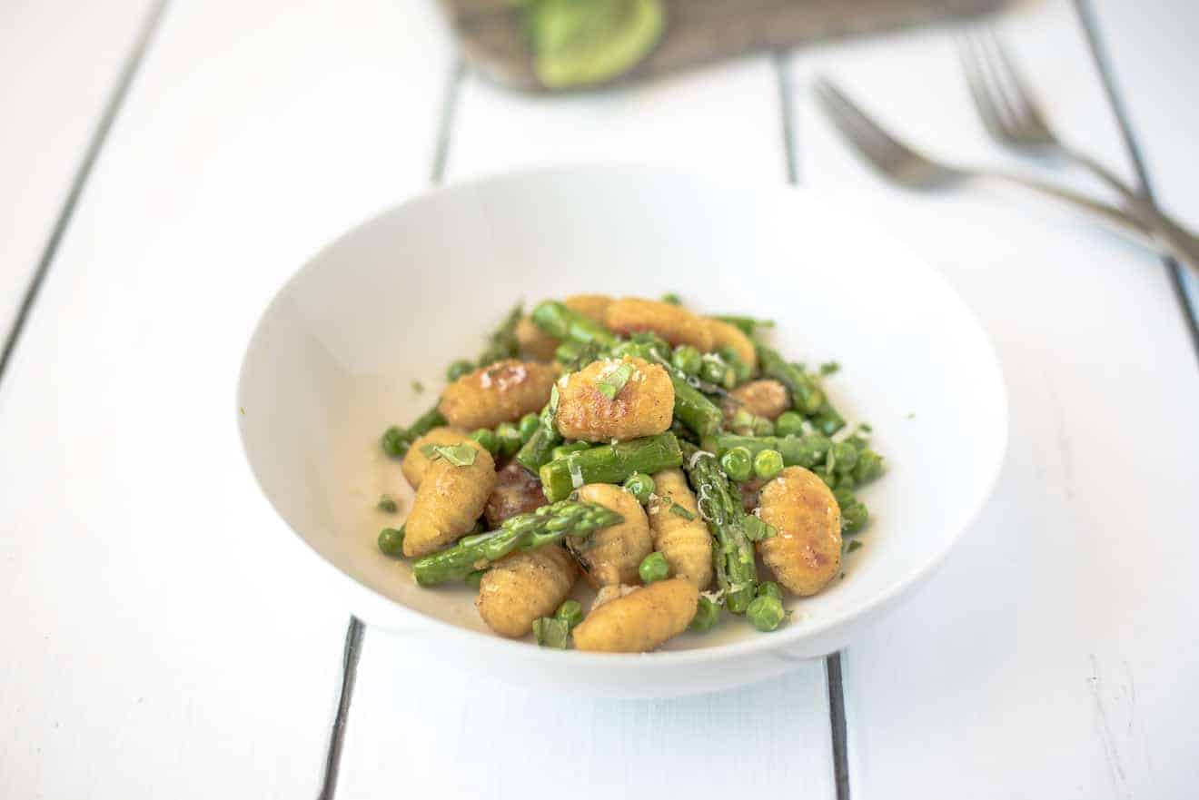 Green asparagus and peas with crispy gnocchi in a white bowl