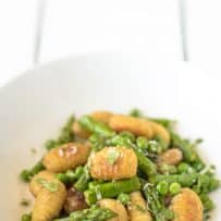 A closeup showing the brown and crispy gnocchi and vibrant green asparagus and peas
