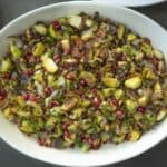 Vibrant green Brussels sprouts in a serving dish garnished with red pomegranate seeds