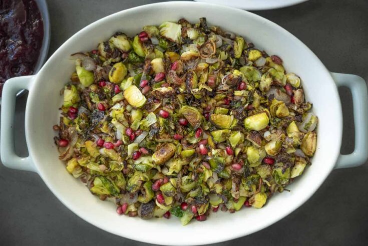 Vibrant green Brussels sprouts in a serving dish garnished with red pomegranate seeds