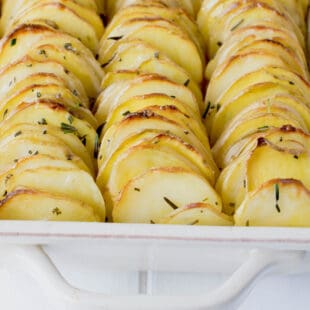 A closeup of thinly sliced potatoes stacked together vertically topped with rosemary