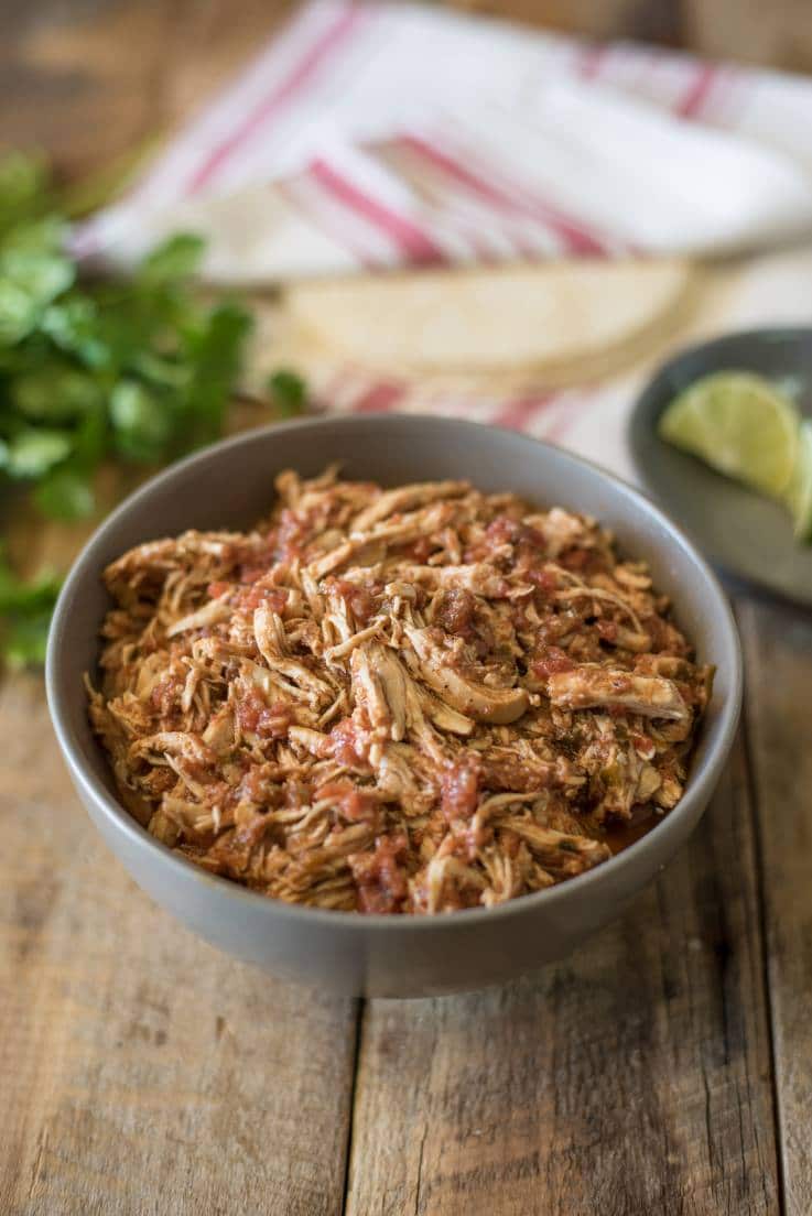 Crockpot Mexican shredded chicken in a grey bowl with cilantro and tortillas