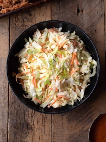 An overhead view of vegetable coleslaw in a bowl with shredded chicken