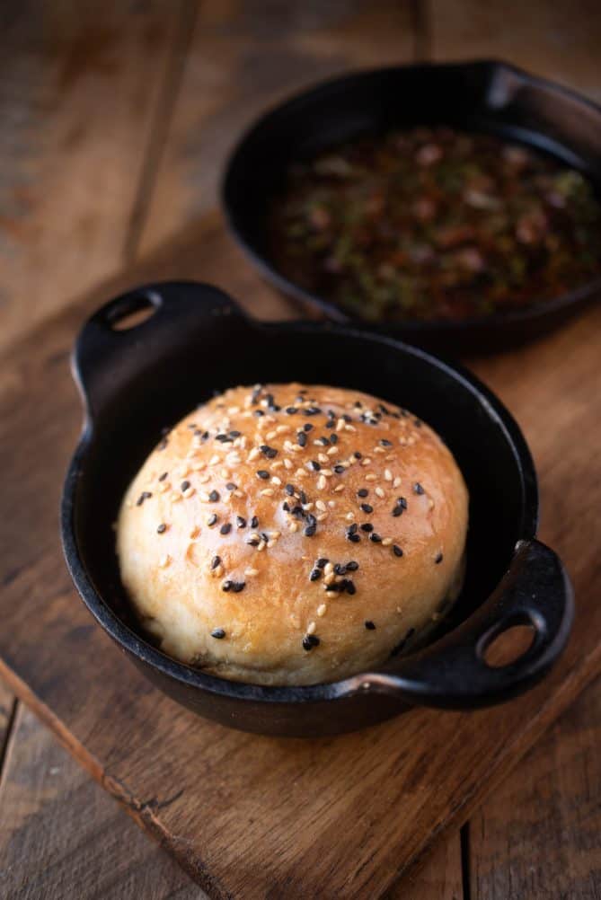 A crusty roll topped with sesame seeds served in a small cast iron bowl