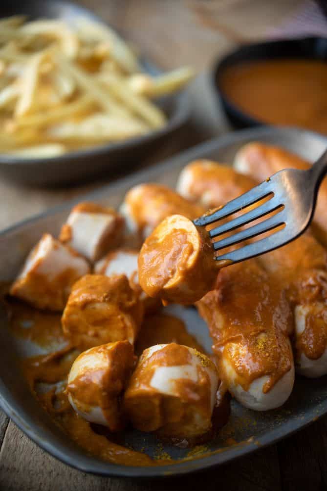 A slice of sausage and currywurst sauce on a fork