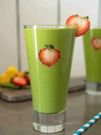 Strawberry slices on the inside of the glass and on the rim of this detox green smoothie