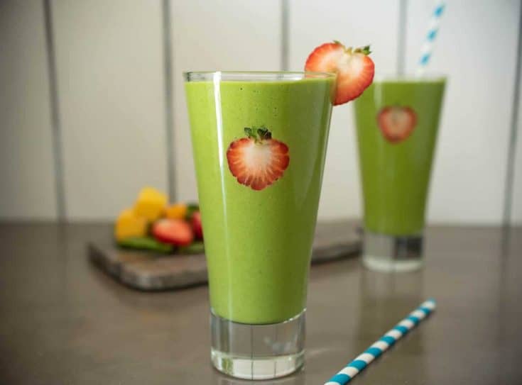 Strawberry slices on the inside of the glass and on the rim of this detox green smoothie