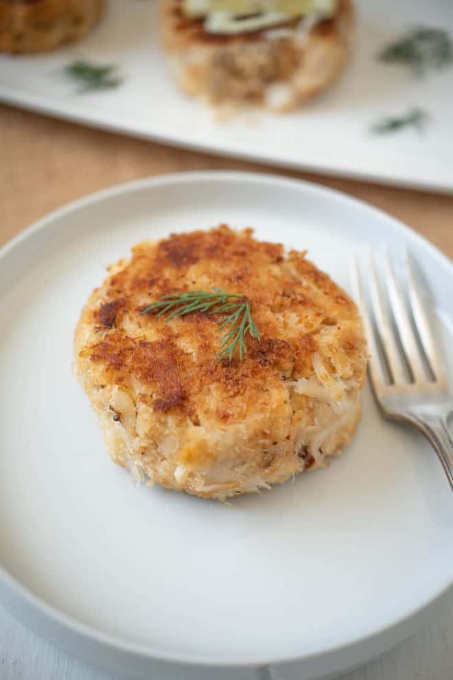 1 crab cake topped with fresh dill on a plate with a fork