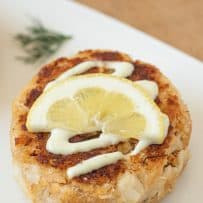 A closeup of a Dungeness crab cake drizzled with sauce and lemon