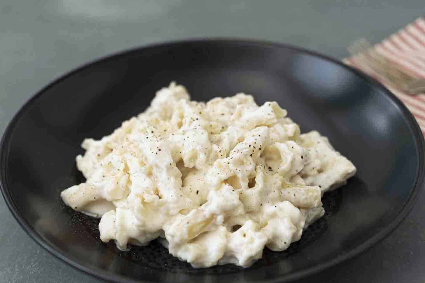 Creamy white sauce and pasta in a black bowl