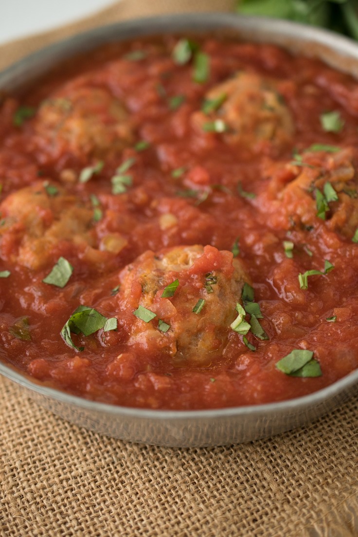 A closeup image of an easy chicken meatball in a pan of marinara sauce
