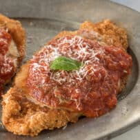 A closeup showing delicious marinara sauce poured over crispy breaded chicken topped with grated Parmesan