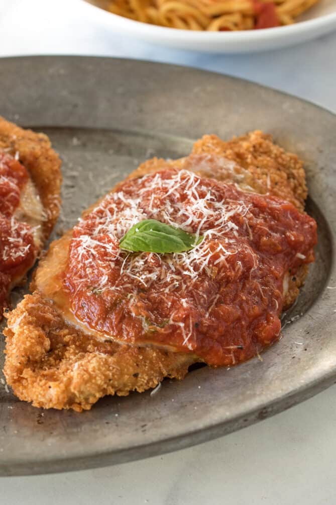 A closeup showing delicious marinara sauce poured over crispy breaded chicken topped with grated Parmesan