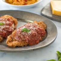 2 breaded and fried chicken breasts topped with marinara sauce and cheese with fresh basil