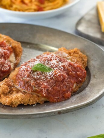 2 breaded and fried chicken breasts topped with marinara sauce and cheese with fresh basil