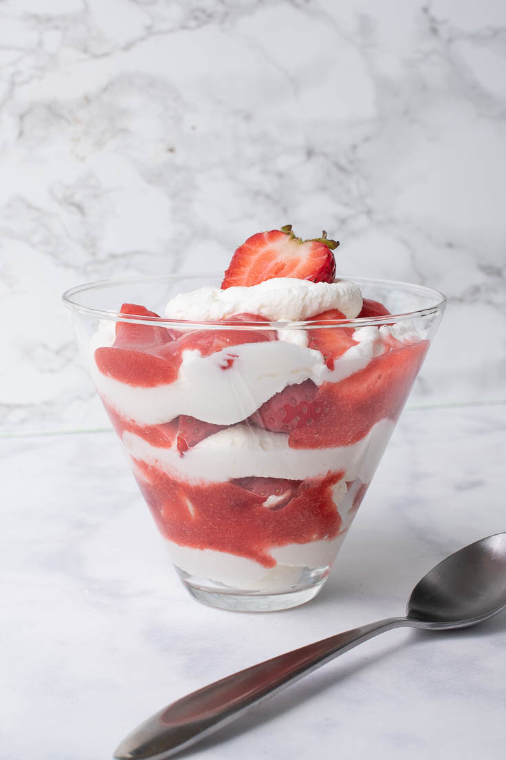 Eton Mess in a glass bowl from the side showing the red and white layers of meringue, whipped cream and strawberries