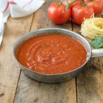 Easy homemade marinara sauce in a skillet with a spoon, fresh basil, spaghetti and fresh tomatoes