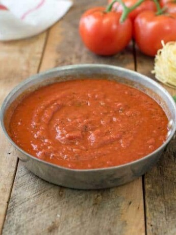 Easy homemade marinara sauce in a skillet with a spoon, fresh basil, spaghetti and fresh tomatoes