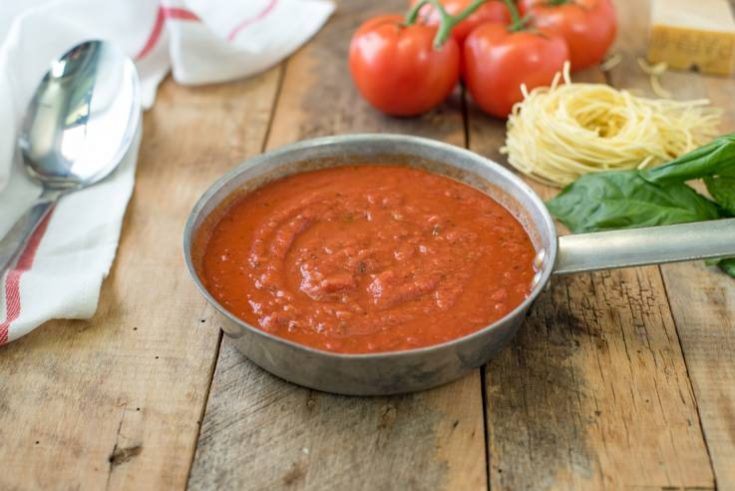 Easy homemade marinara sauce in a skillet with a spoon, fresh basil, spaghetti and fresh tomatoes