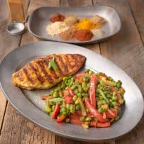 A oval plate with a grilled chicken breast with Indian spices peas