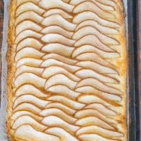 A whole pear tart on a baking sheet with the pear slices in a fan design